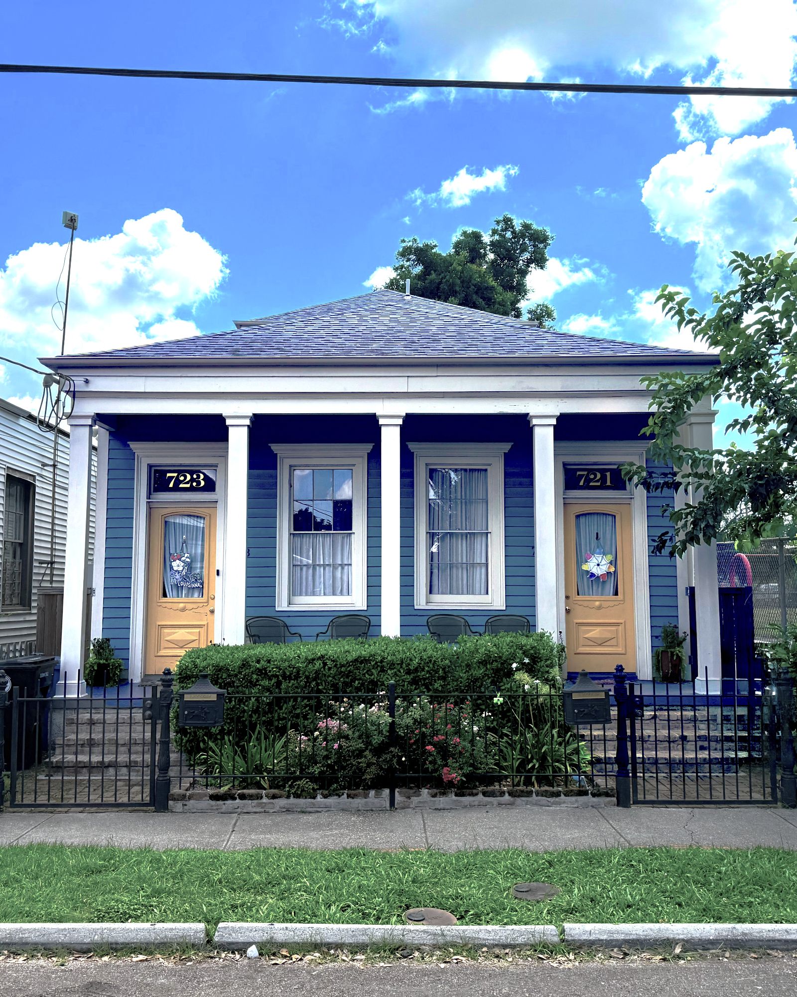 Delachaise Duplex — blue weatherboard double with twin yellow doors, columned porch, and ironwork fence in front.